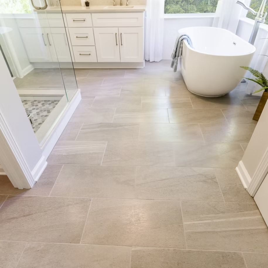 Bright bathroom with light wood tile floor, white vanity, glass shower, and freestanding tub by a window
