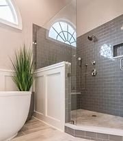 Modern bathroom with white vanity, glass shower, gray tile, and potted plant
