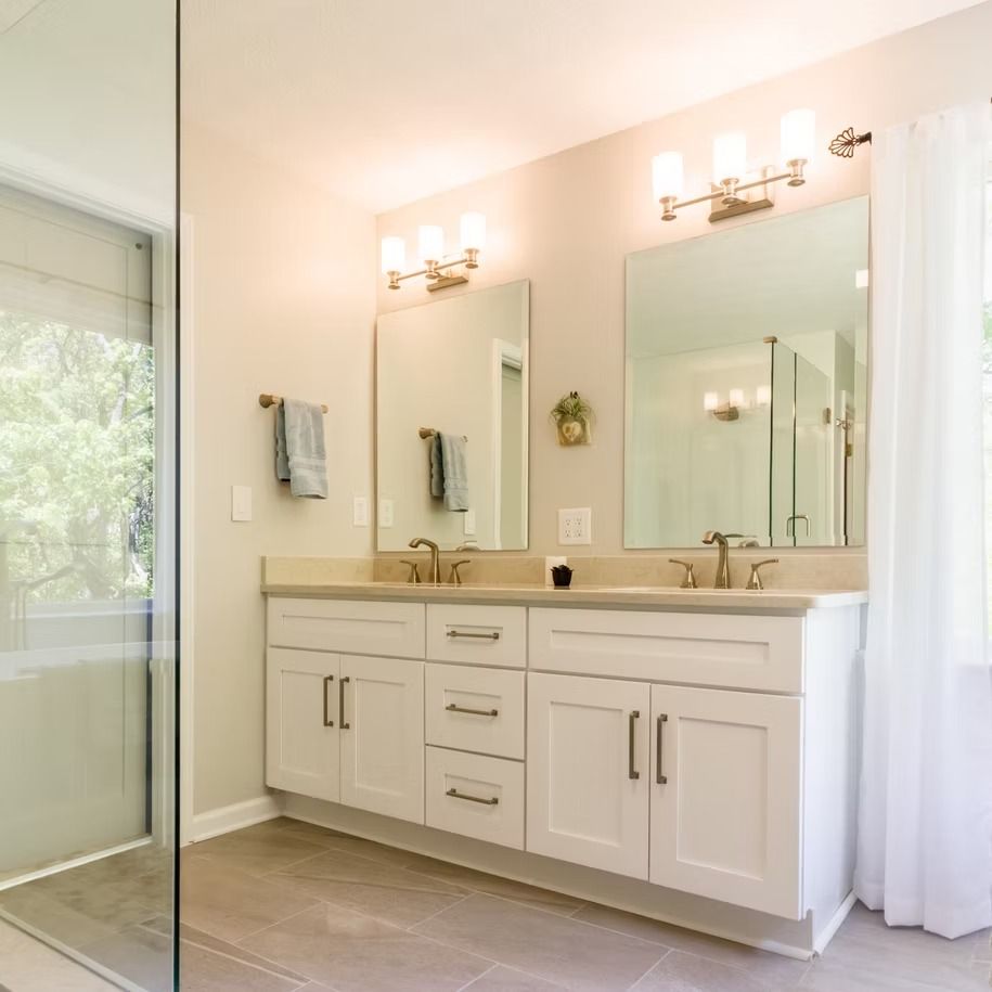 Bright modern bathroom with white double vanity, large mirror, sconces, and glass shower door