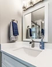 Bright bathroom vanity with white countertop, rectangular mirror, chrome faucet, and blue towels.