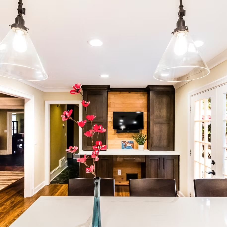 Modern kitchen and dining area with pendant lights, white island, and a wall-mounted TV above wood cabinets