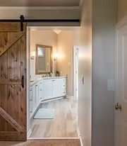 Sliding barn door opens to a bright bathroom with a white vanity and mirror.