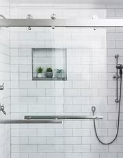 Minimal white-tiled shower with built-in shelf, glass window ledge, and handheld showerhead on the right.