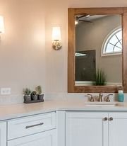 Bathroom vanity with white cabinets, mirror, wall sconce, and small plants on a countertop