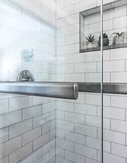 Glass shower door with chrome handle and white subway tile walls in a bathroom