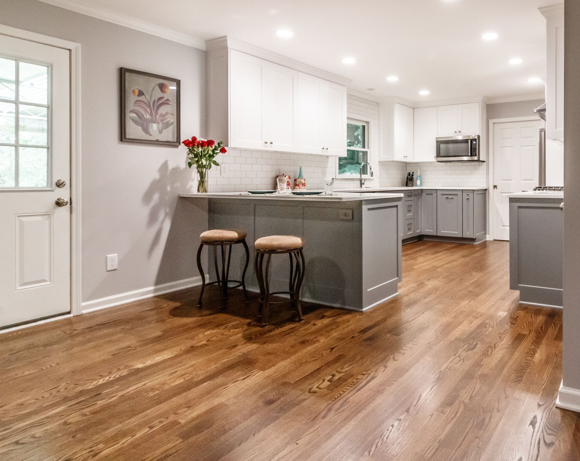 Bright modern kitchen with white cabinets, gray island, hardwood floors, and two bar stools