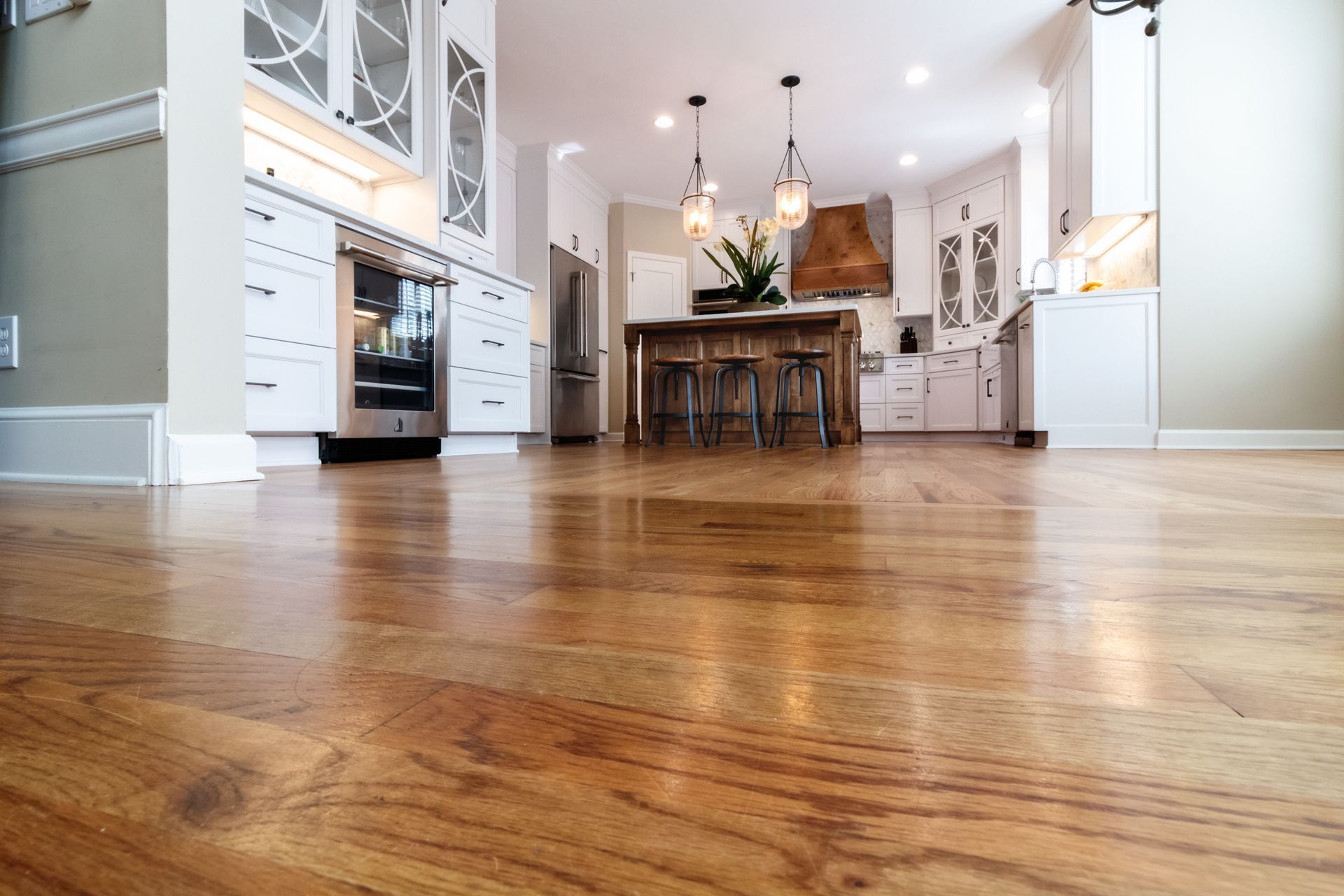 Modern kitchen and dining area with hardwood floors, white cabinets, and a kitchen island with pendant lights.