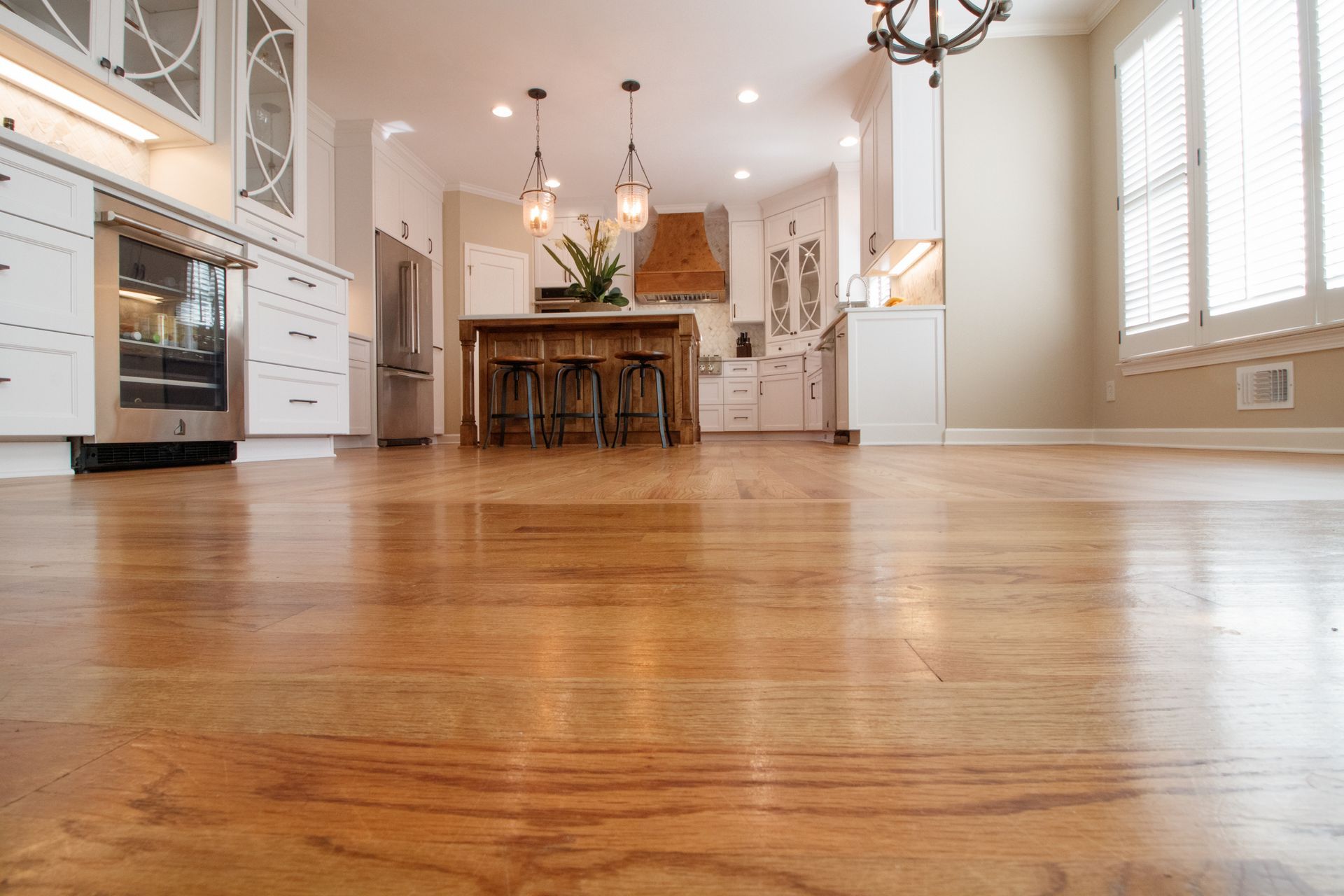 Bright open kitchen with hardwood floors, white cabinets, island, and bar stools under pendant lights