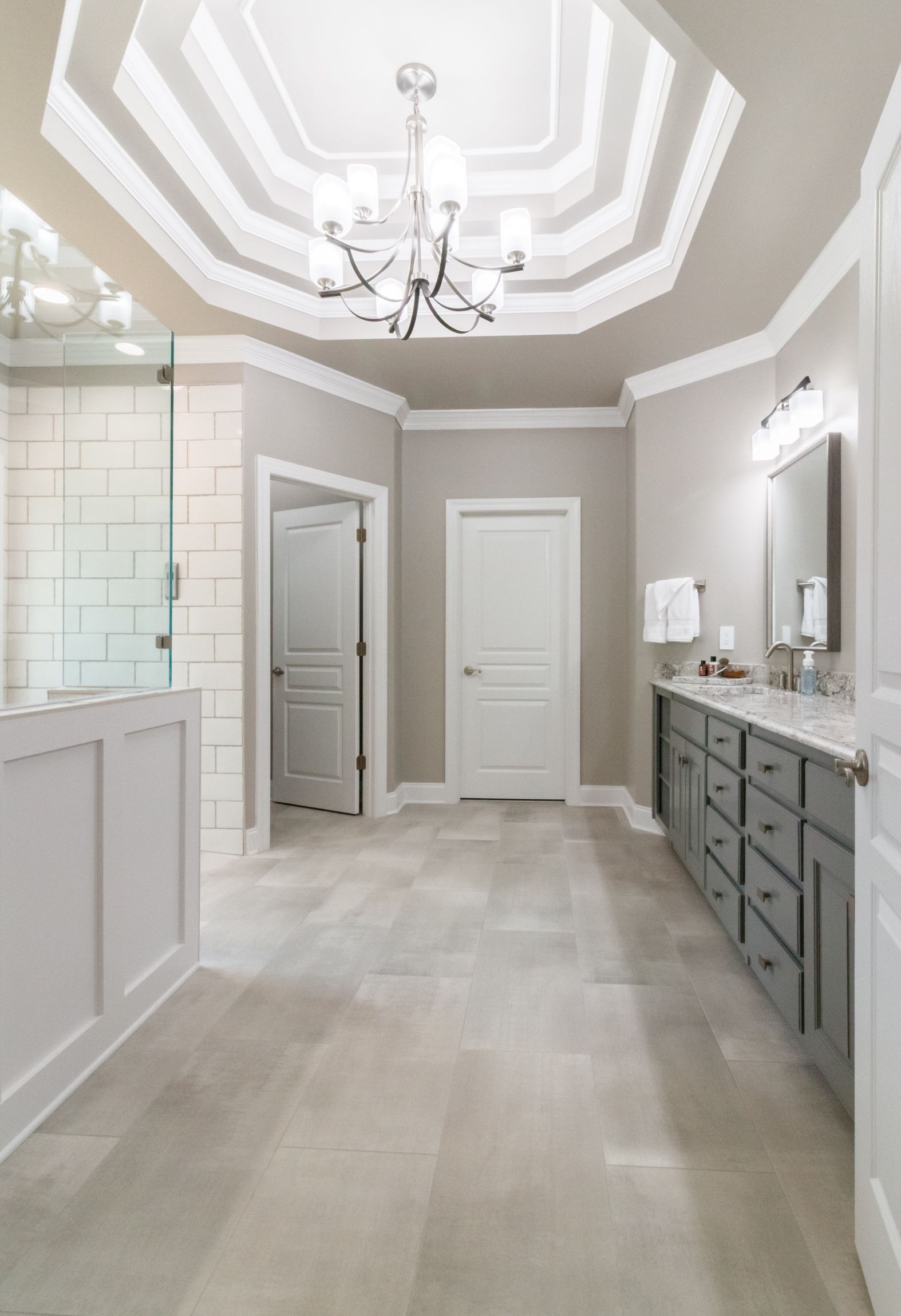 Bright modern bathroom with gray vanity, large mirror, and octagonal tray ceiling with chandelier
