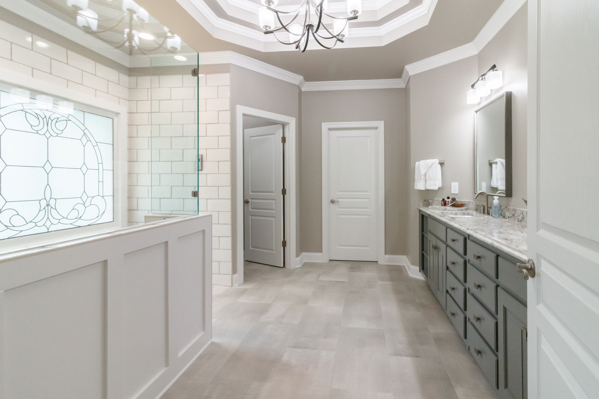 Elegant white and gray bathroom with a glass shower, double vanity, and tall arched ceiling