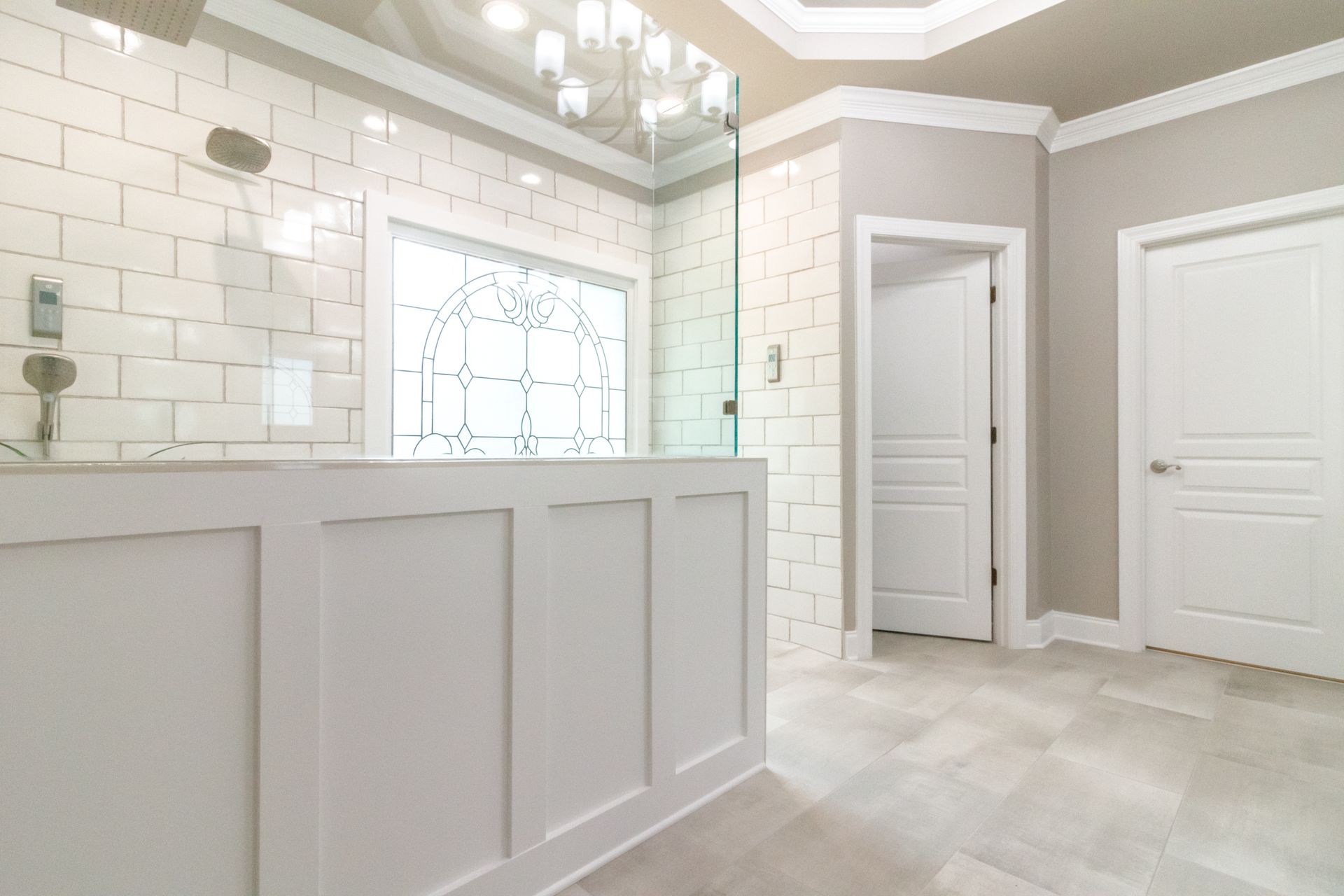 Bright white bathroom with glass shower, tiled walls, and paneled vanity cabinets