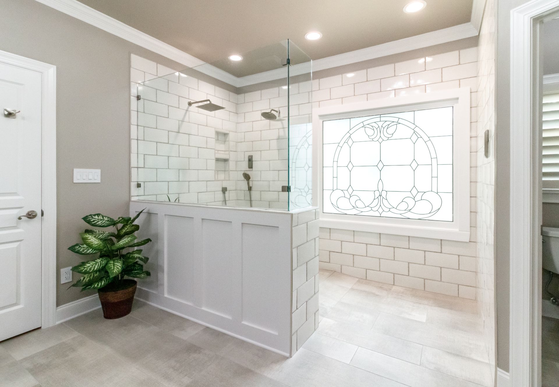 Bright modern bathroom with white tile, glass shower, and decorative window.
