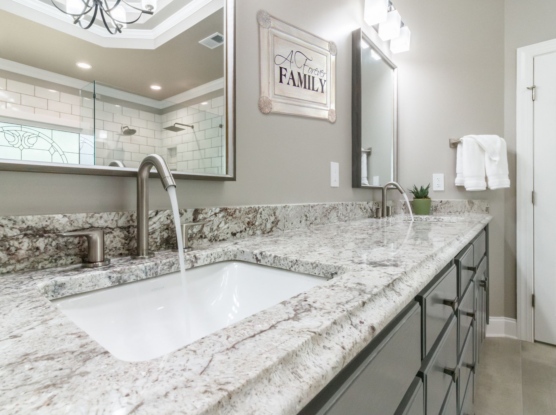 Bright bathroom vanity with granite countertop, undermount sink, mirror, and towel bar by a shower door