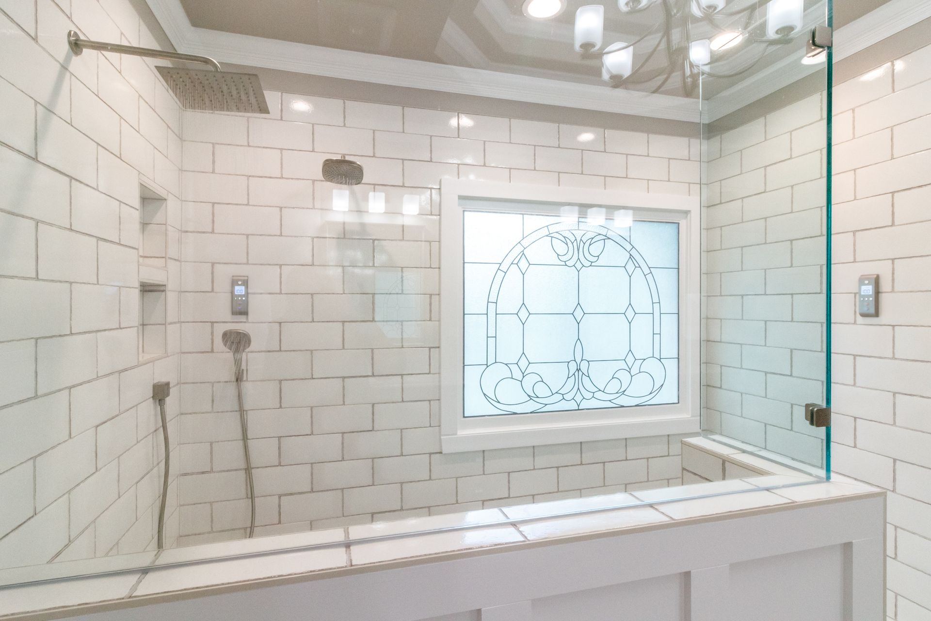White-tiled bathroom with a glass shower and frosted window behind a white vanity.