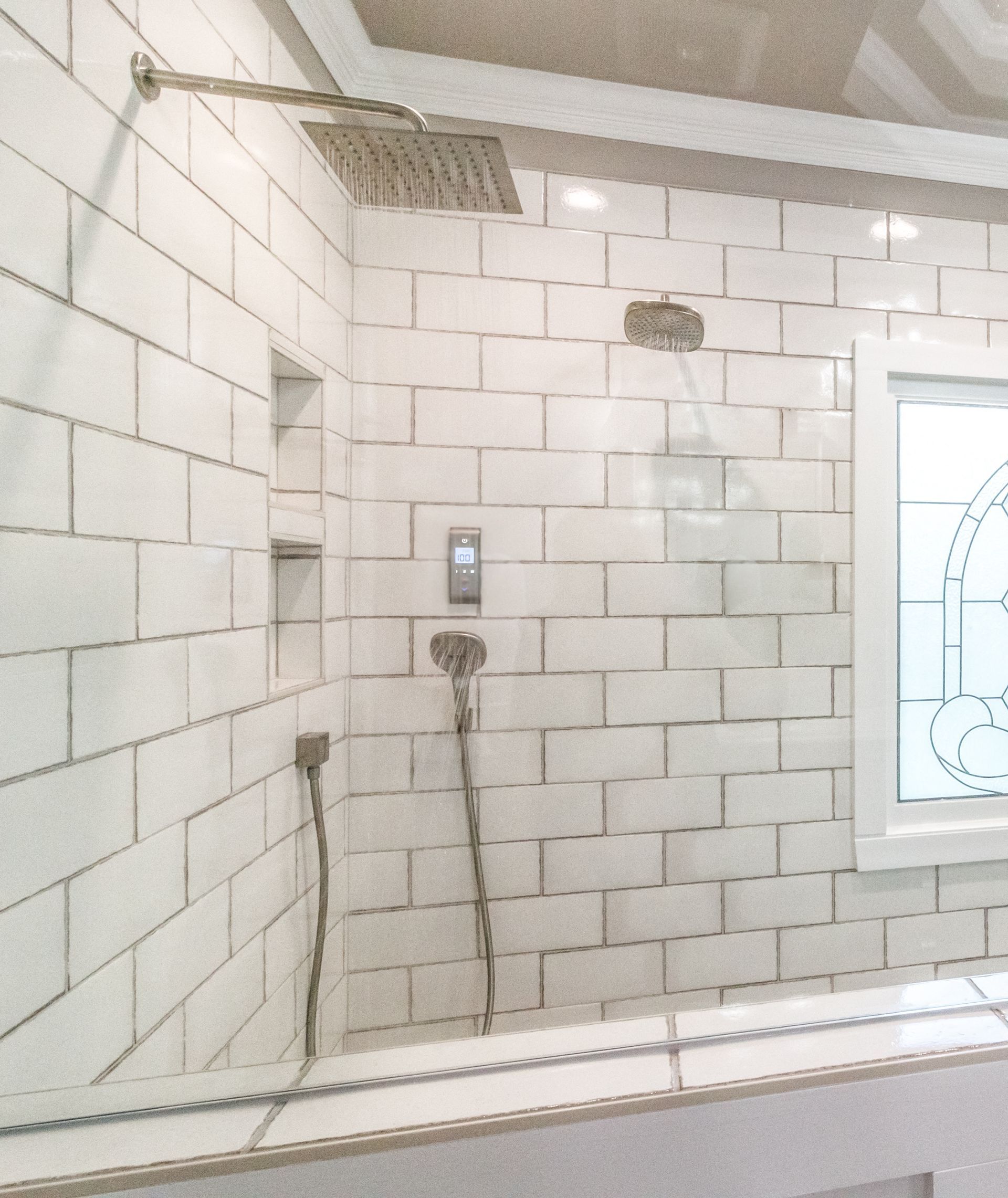 Bathroom shower stall with white tiled walls, exposed shower head, and wall fixtures.
