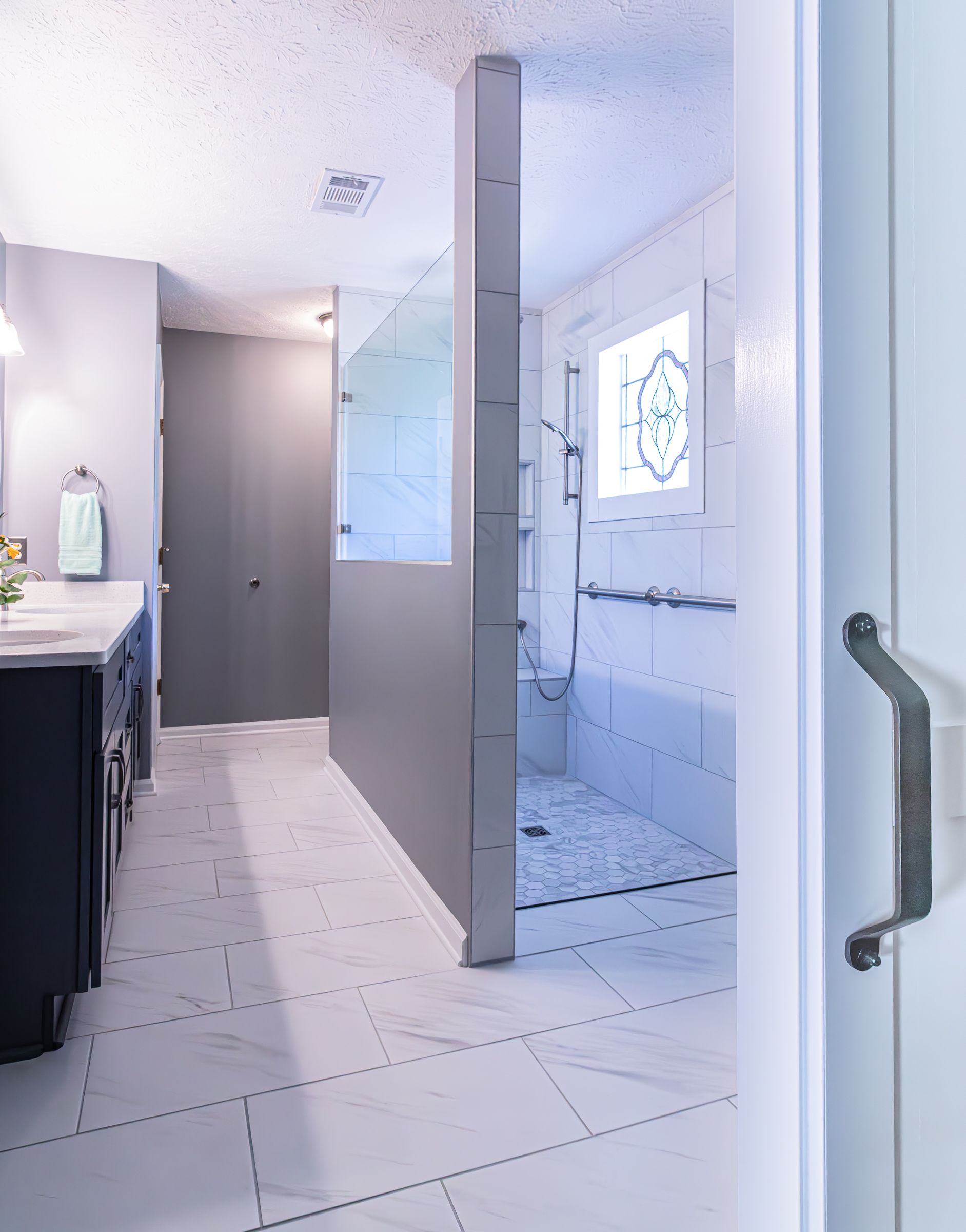 Bright bathroom with white tile, shower stall, and sink vanity near an open door