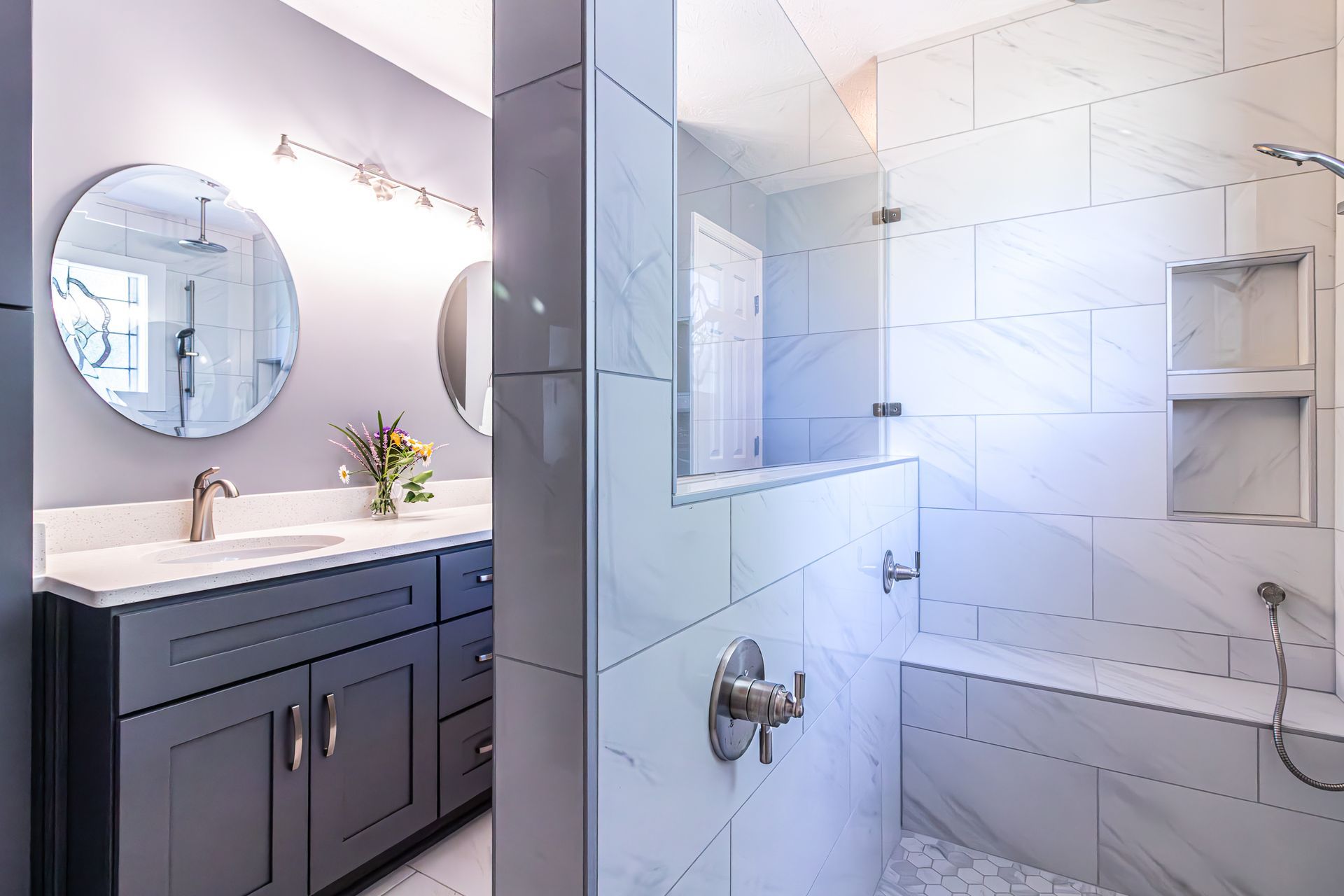 Modern bathroom with dark vanity, round mirror, and glass shower enclosure