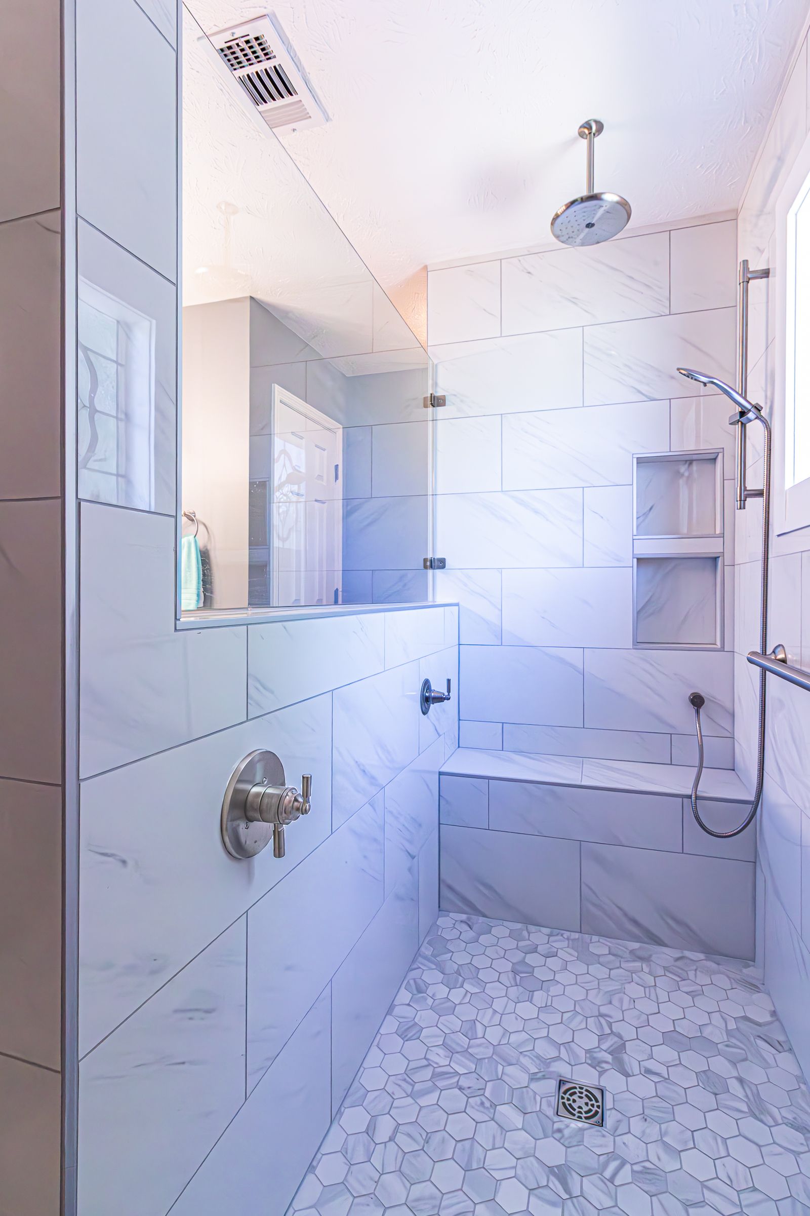 Modern white tiled walk-in shower with rain showerhead, bench, and handheld sprayer
