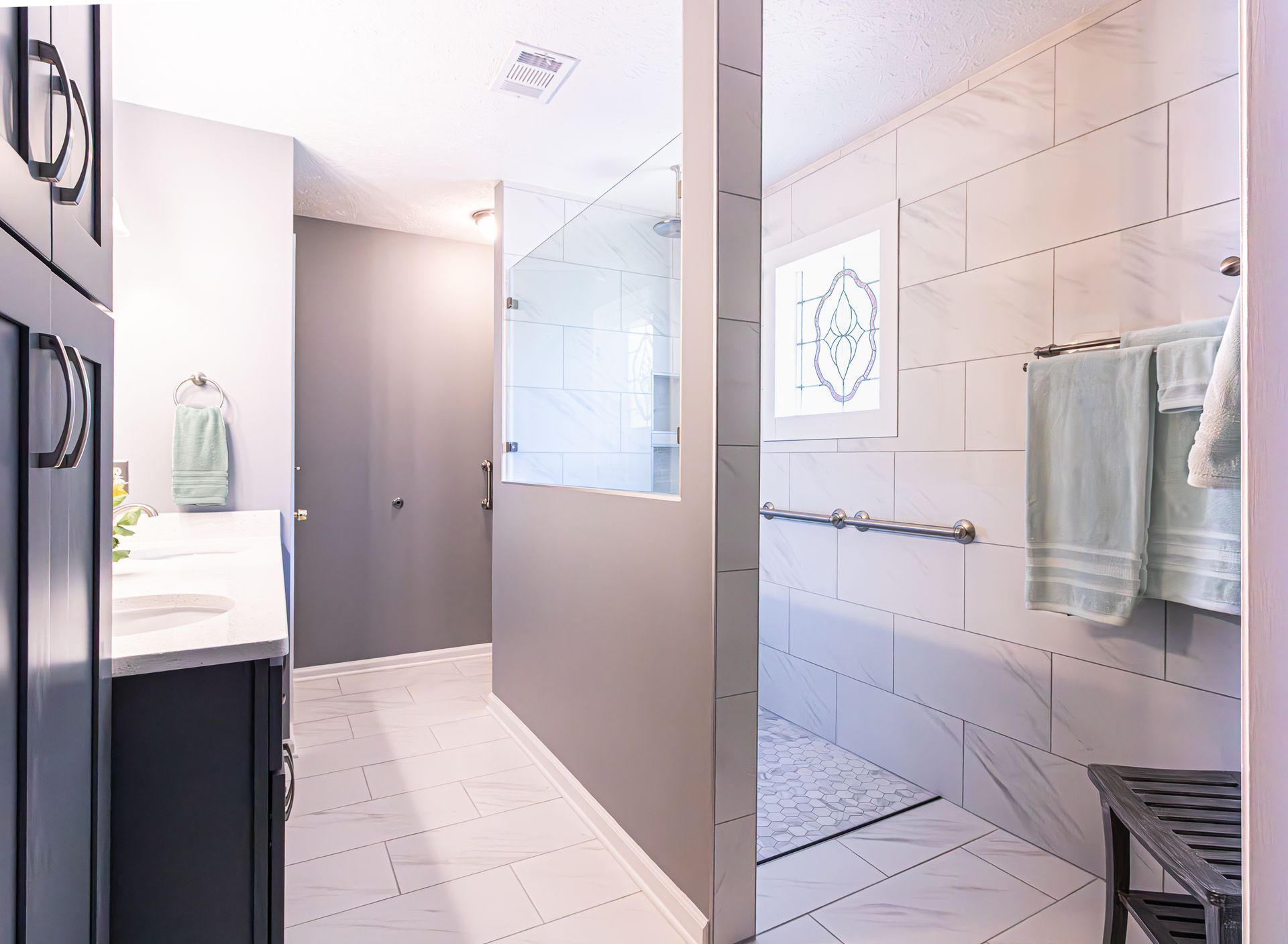 Modern bathroom with glass shower, white tile, sink vanity, and towel rack