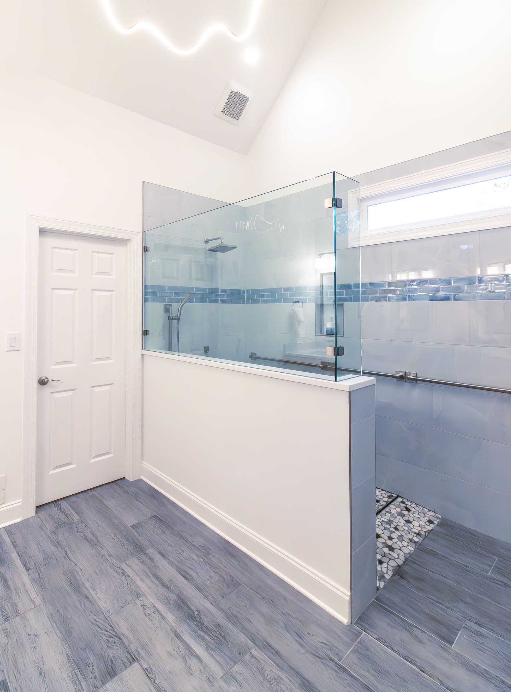 Bright bathroom with frosted glass shower, blue-gray tile, and white walls and door.