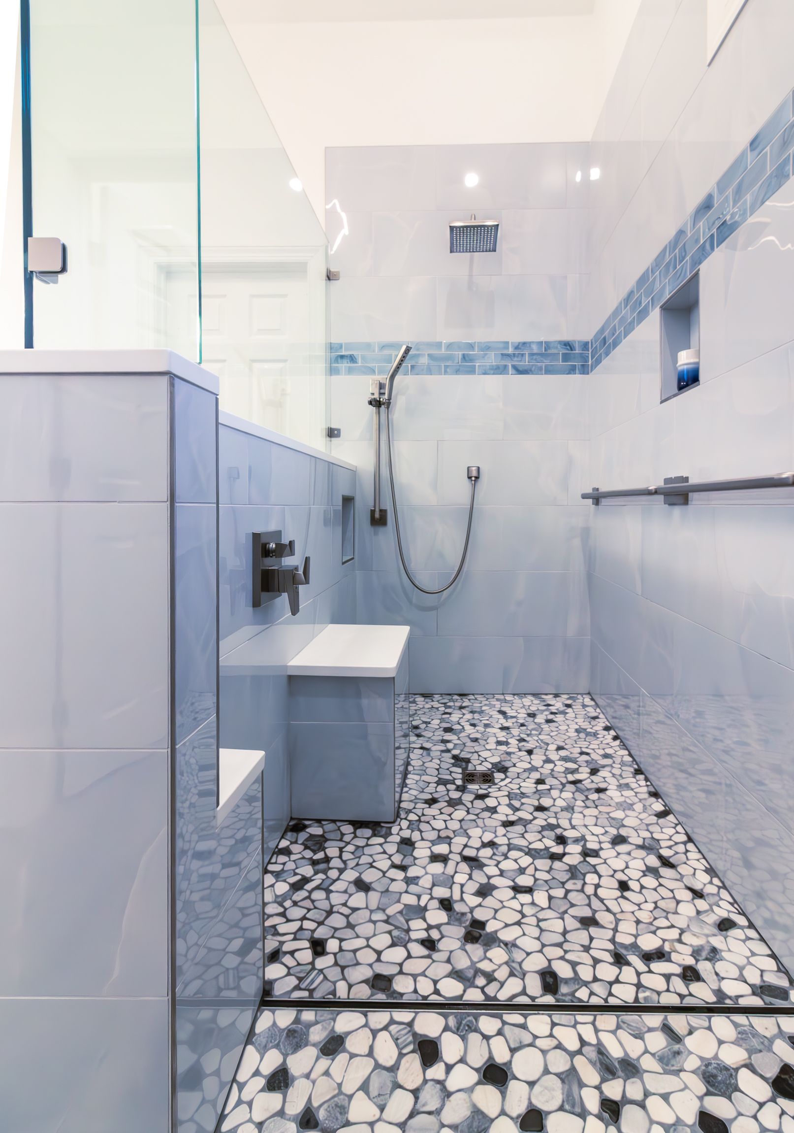 White tiled bathroom with a walk-in shower, grab bars, and pebble-pattern floor.