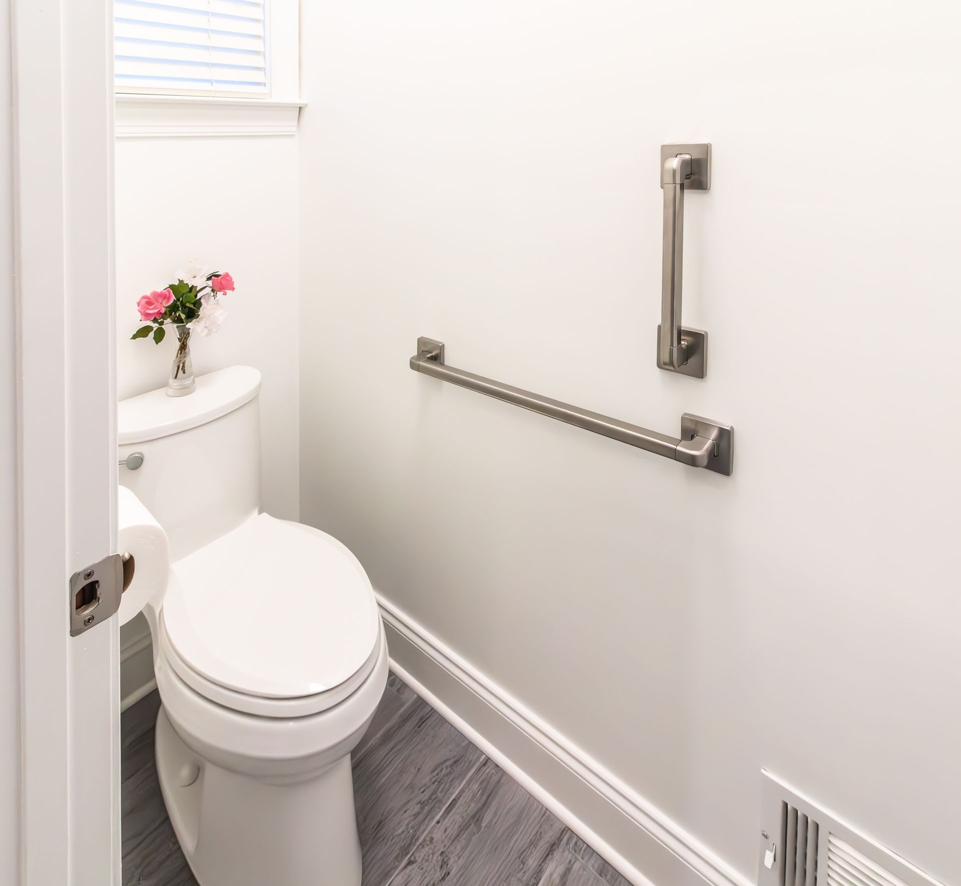 Accessible bathroom with toilet, grab bars, and a small flower vase on the tank