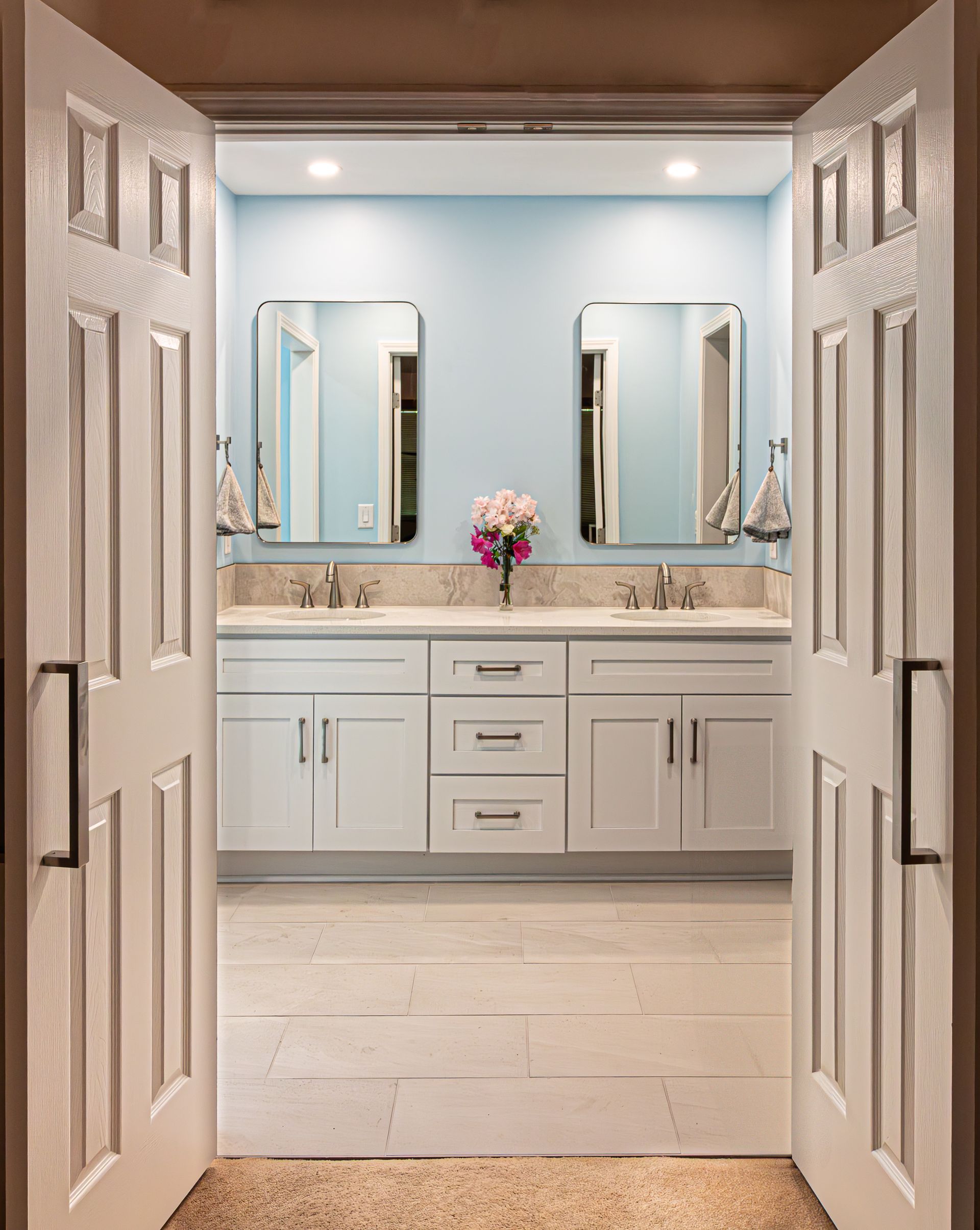 White double vanity bathroom with mirrors, light blue walls, and open doors framing the view