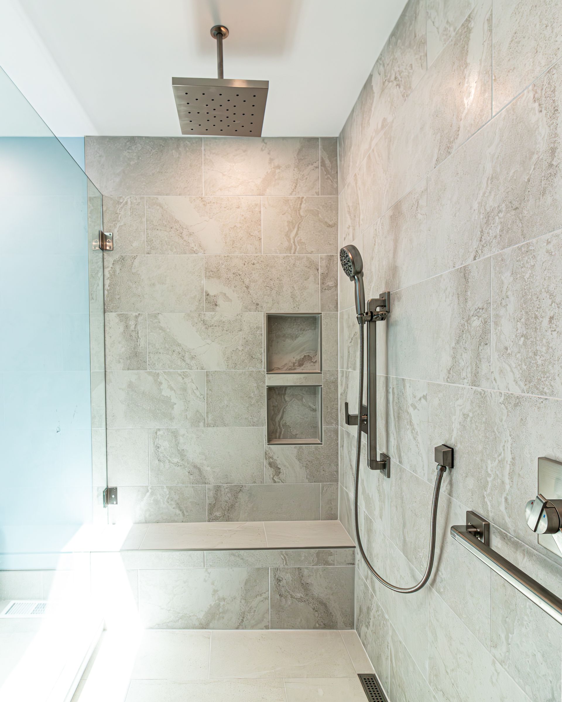 Modern walk-in shower with stone tile, rainfall showerhead, handheld spray, and built-in niches
