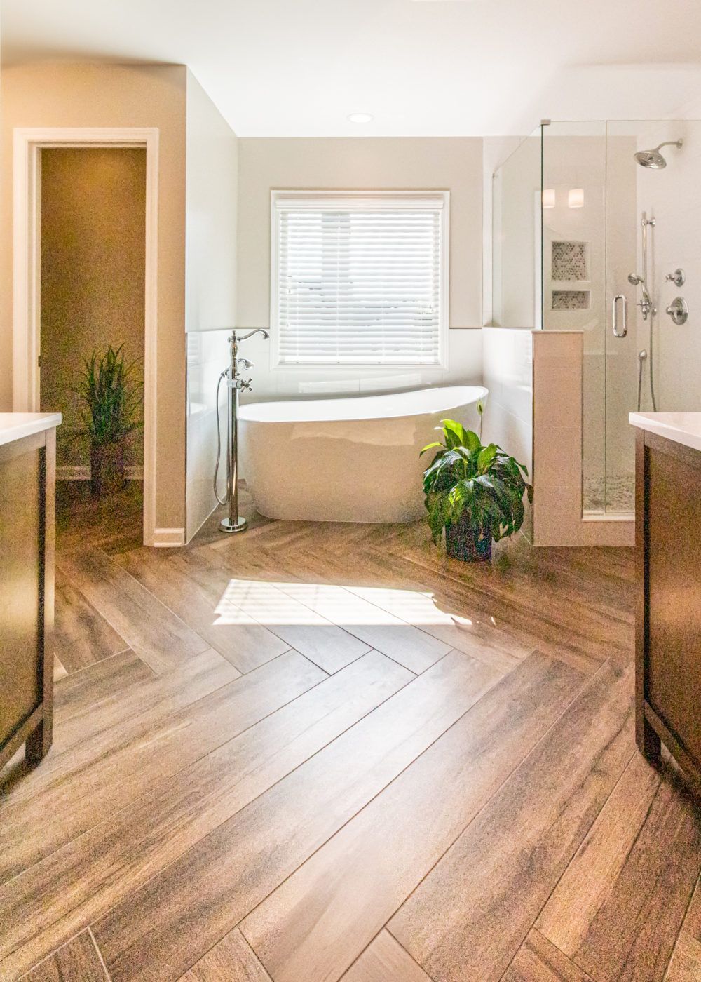 Bright bathroom with a bathtub, glass shower, window blinds, and wood-look flooring.