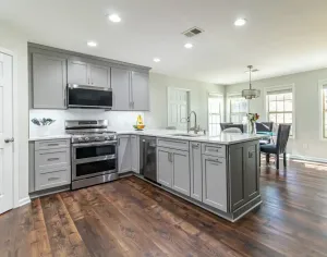 Bright modern kitchen with gray cabinets, stainless steel appliances, and hardwood floors, open to a dining area