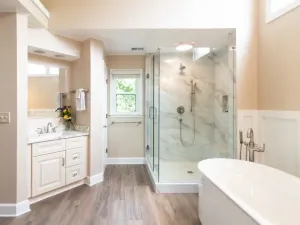 Bright bathroom with vanity, glass walk-in shower, and freestanding tub with marble walls and wood-look flooring
