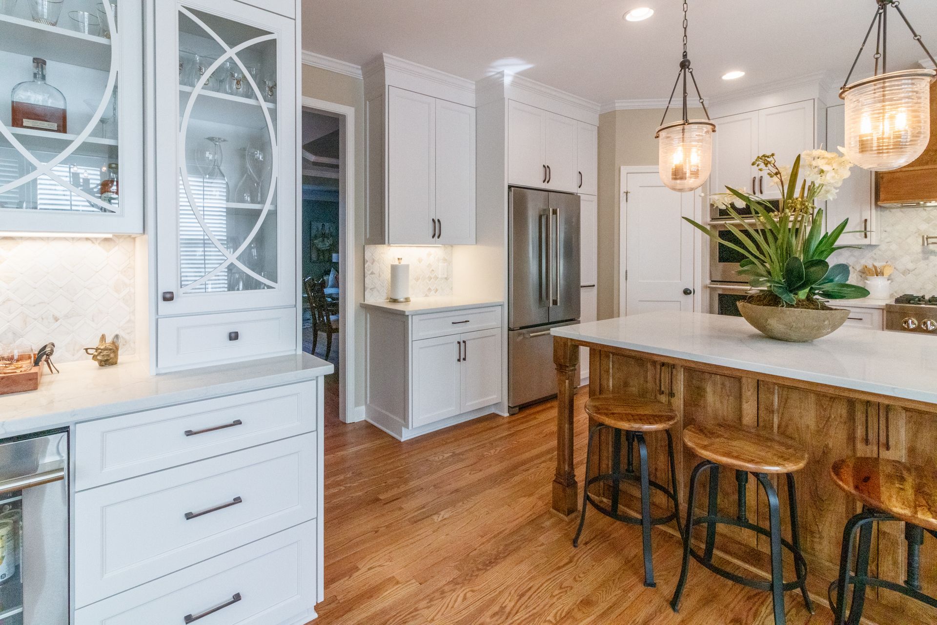 Bright modern kitchen with white cabinets, wood island, stools, and pendant lights