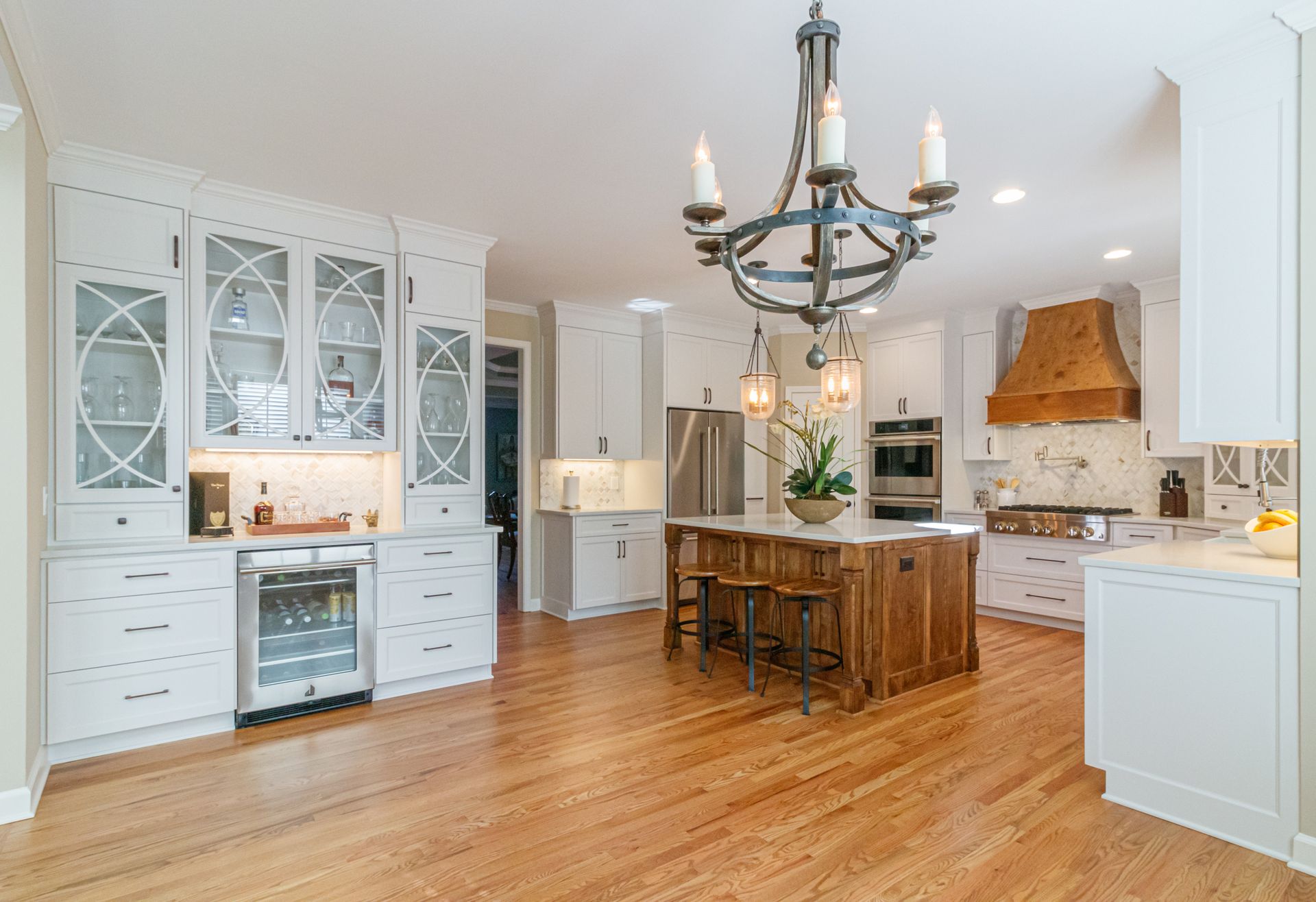 Spacious white kitchen with wooden island, chandelier, tiled backsplash, and hardwood floors