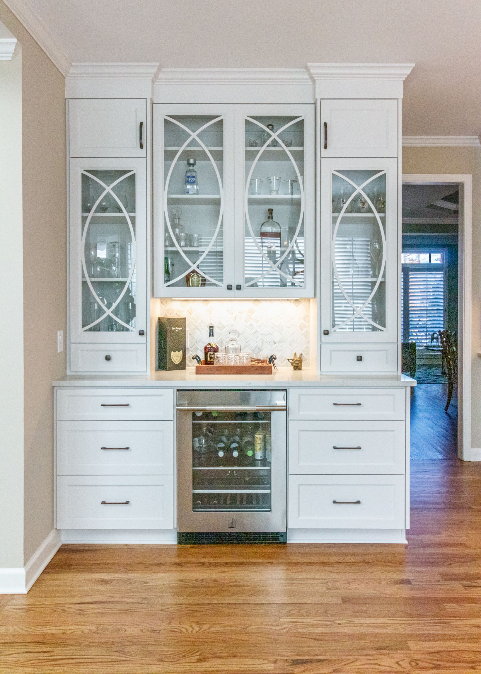 White kitchen built-in with glass-front cabinets, wine cooler, and hardwood floor.