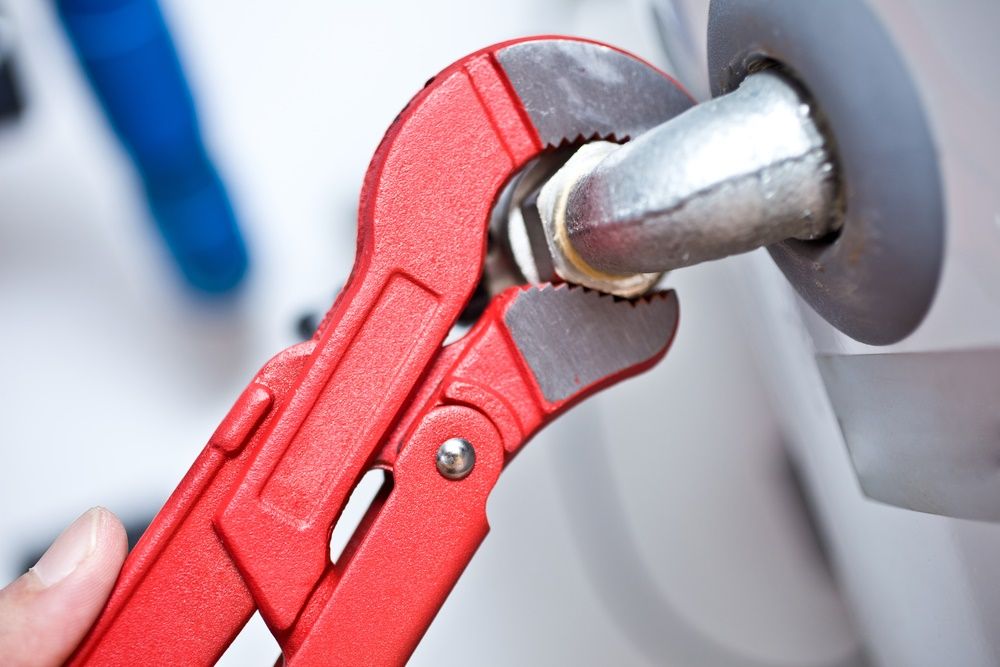 A Person Is Fixing A Water Heater With A Wrench — Edwards Plumbing Pty Ltd in Chillingham, NSW