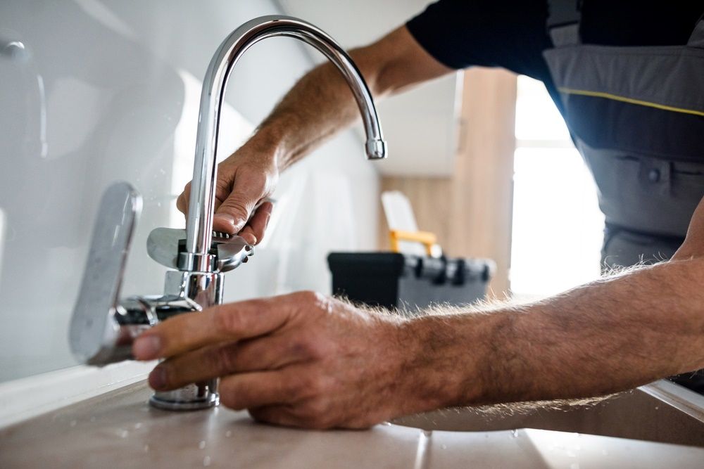 A Man Is Fixing A Faucet In A Bathroom — Edwards Plumbing Pty Ltd in Byrrill Creek, NSW