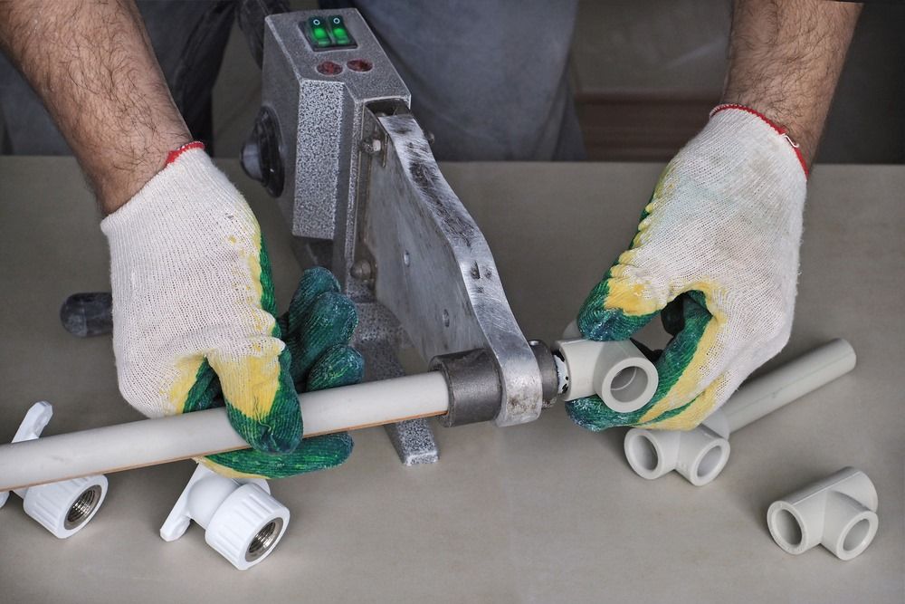 A Man Is Cutting A Plastic Pipe With A Machine — Edwards Plumbing Pty Ltd in Burringbar, NSW