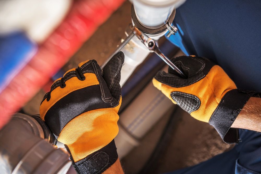 A Man Wearing Yellow And Black Gloves Is Fixing A Pipe With A Wrench — Edwards Plumbing Pty Ltd in Kingscliff, NSW