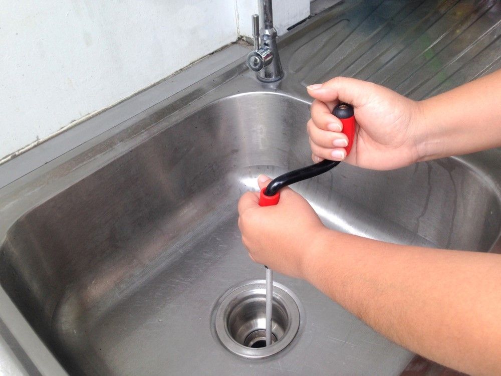 A Person Is Using a Snake to Unblock a Sink Drain — Edwards Plumbing Pty Ltd in Tyalgum, NSW
