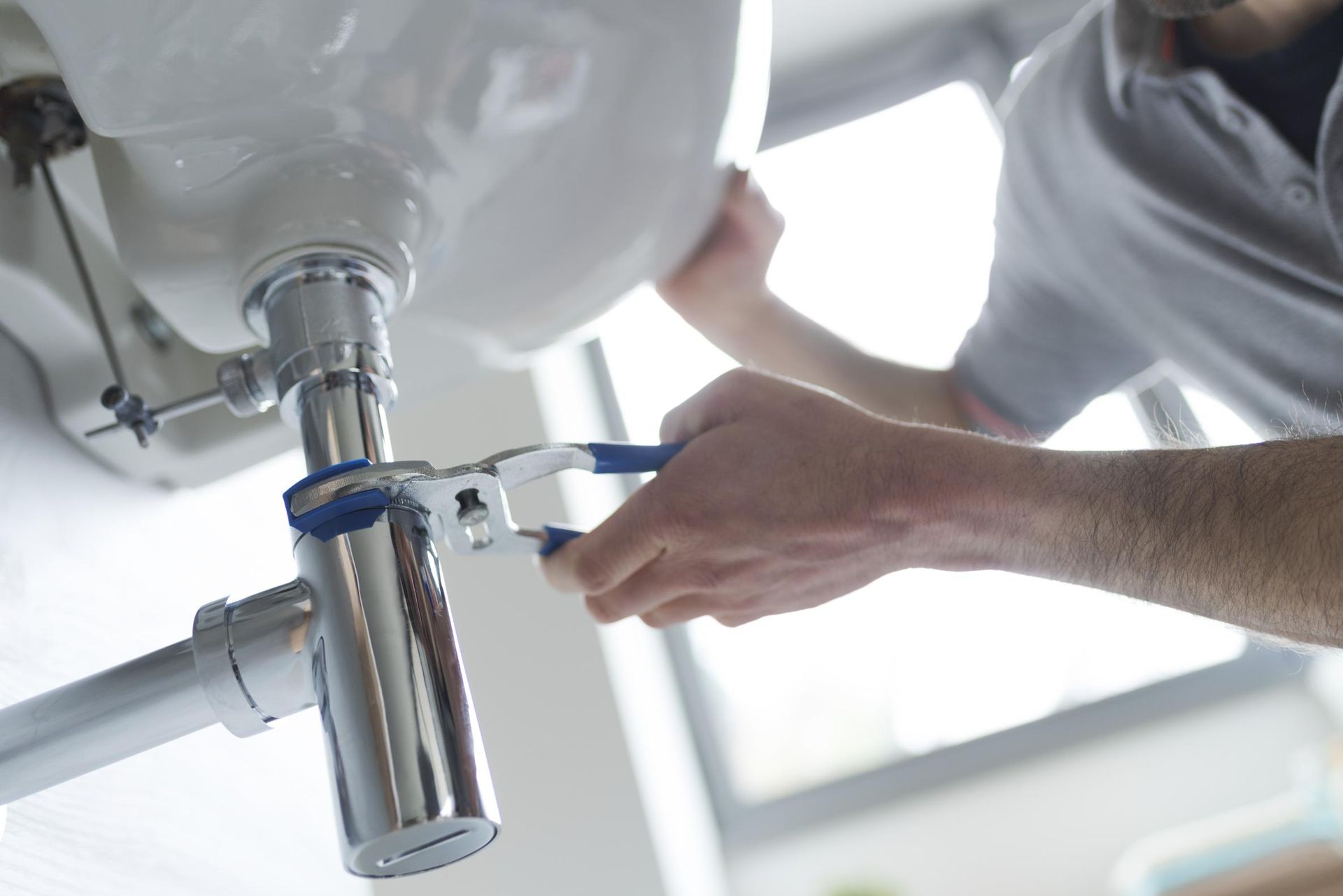 A Man is Fixing a Sink With a Wrench — Edwards Plumbing Pty Ltd in Uki, NSW