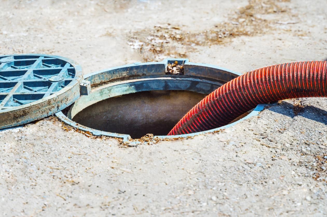 A Manhole Cover With a Red Hose Coming Out of It — Edwards Plumbing Pty Ltd in South Murwillumbah, NSW