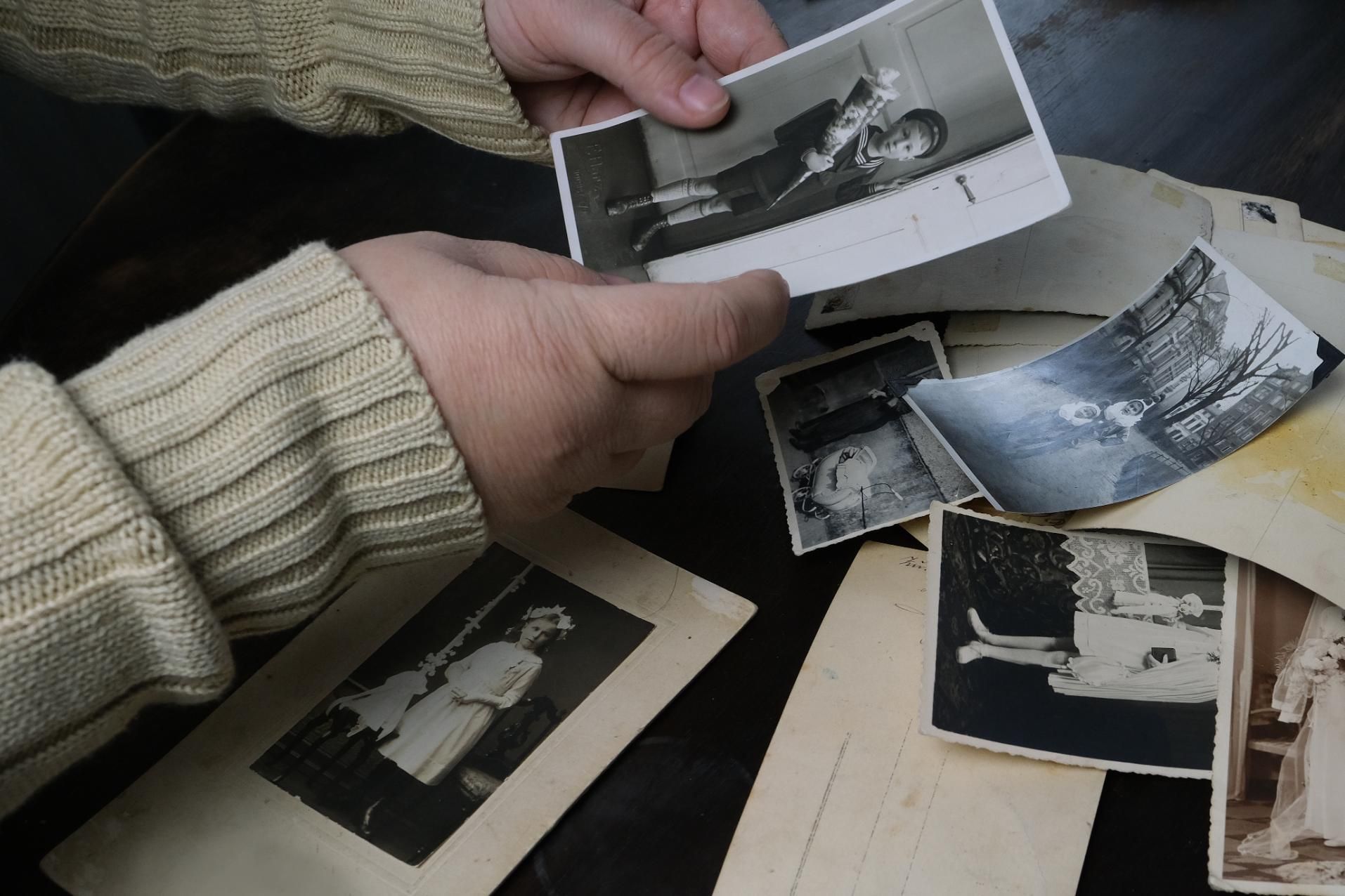 Hands in a cream-colored sweater hold and sort through a collection of vintage black-and-white photographs.