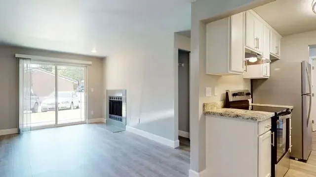 Living room with fireplace and view of sliding glass doors, adjacent to a kitchen with stainless steel appliances.