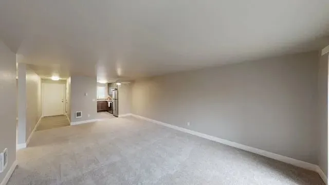 Spacious living area with neutral carpeting and an open kitchen.