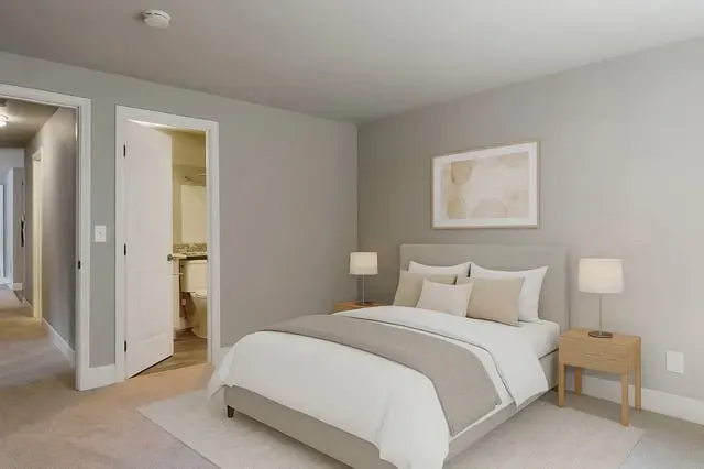 A beautifully staged bedroom with a queen-size bed, nightstands, and a door leading to a bathroom.