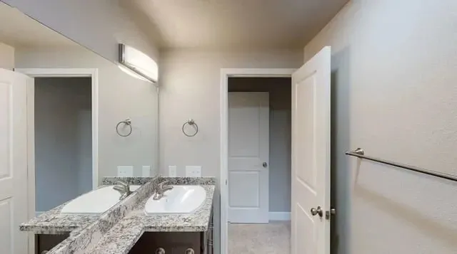 A modern bathroom featuring a double vanity with granite countertops and a large mirror.