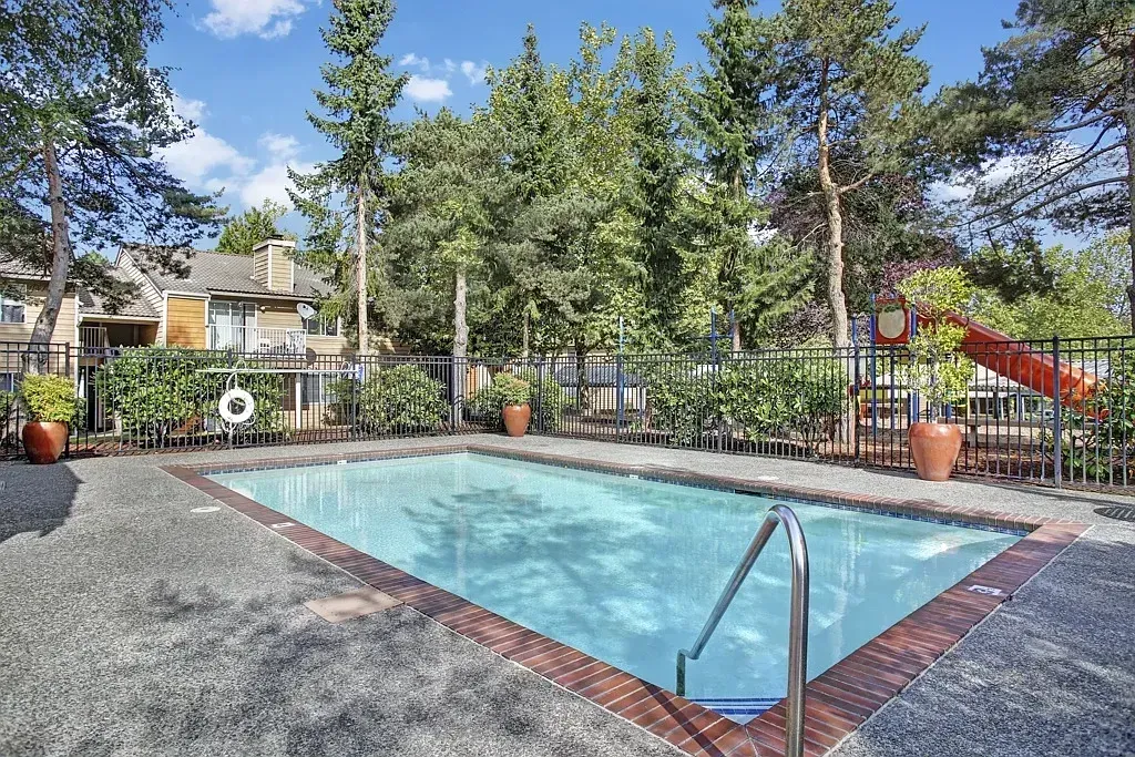 Outdoor swimming pool with blue water, stone deck, and trees under a sunny sky at Larch Alderwood in Lynnwood, WA.