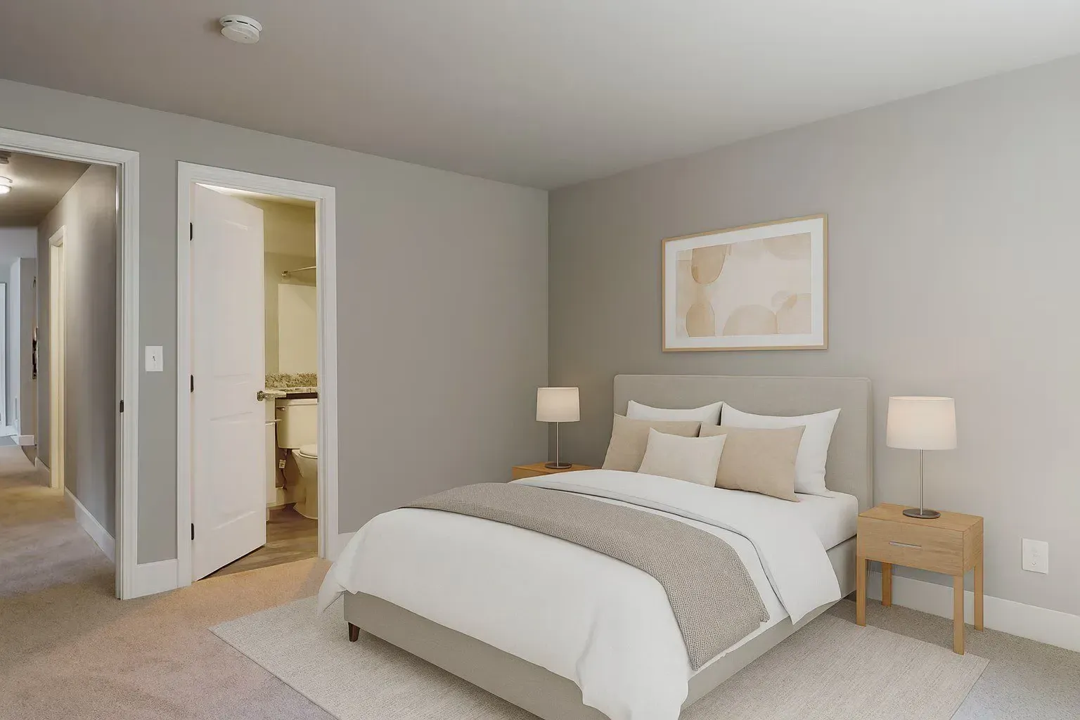 Bright modern bedroom with a bed, bedside lamps, and an open doorway to a bathroom at Larch Alderwood in Lynnwood, WA. 