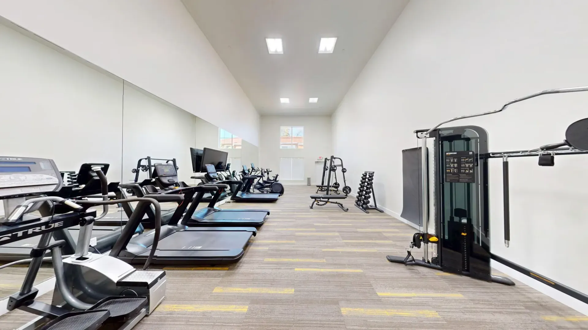 Bright gym interior with treadmills, exercise machines, and mirrors along a long hallway-like room at Larch Alderwood.