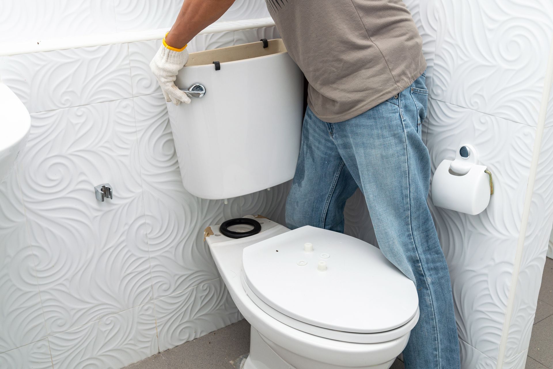 Person installing a white toilet tank in a tiled bathroom